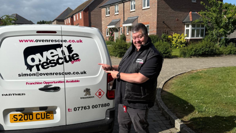 A smiling man in Oven Rescue uniform pointing at an Oven Rescue van