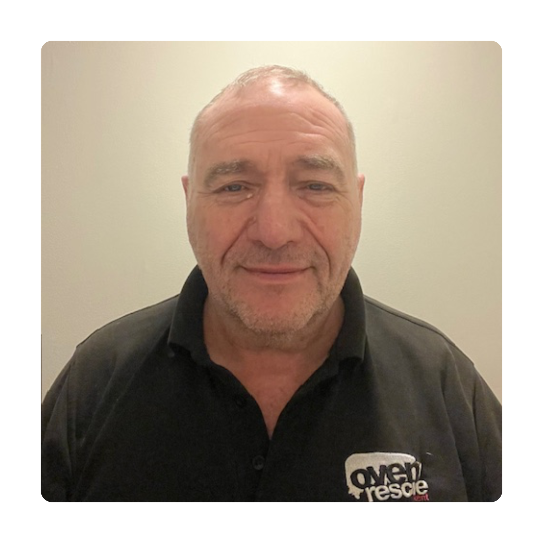Middle-aged man with short hair and a slight smile wearing a black polo shirt with an "oven rescue" logo. Plain background conveys simplicity.