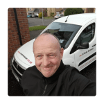 A person smiling in front of a white van with "ovenrescue.co.uk" and a contact number on it, parked in a suburban neighborhood driveway.
