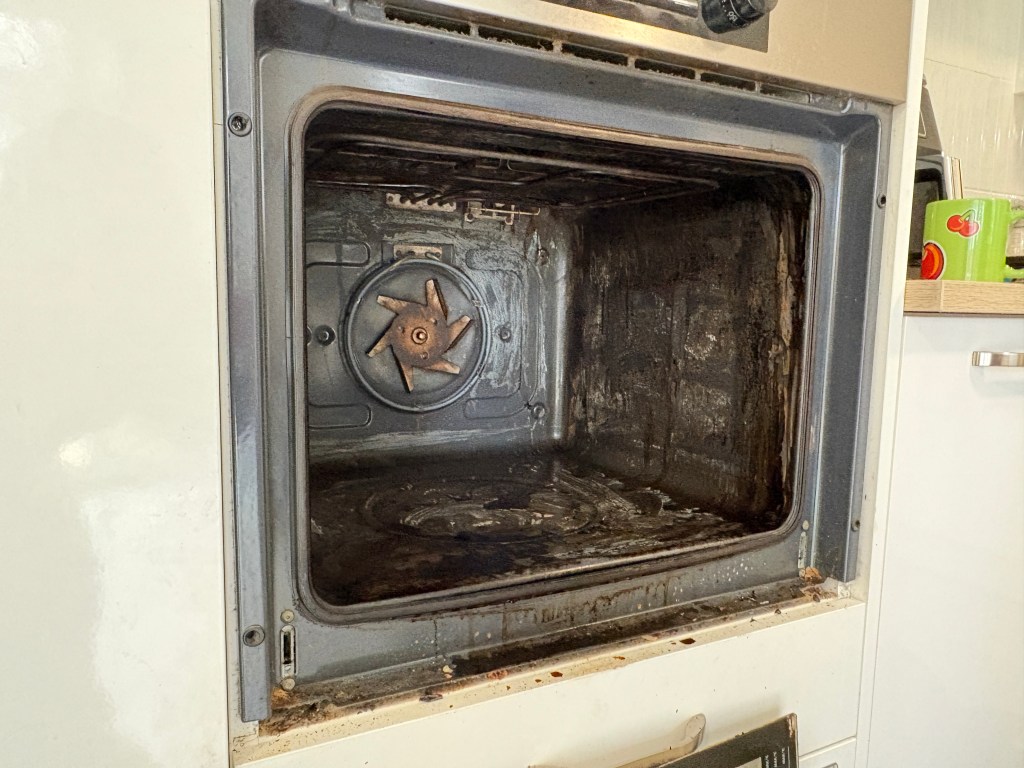A dirty, well-used oven interior with grease and grime on the metal surfaces, conveying a neglected and unkempt kitchen appliance.