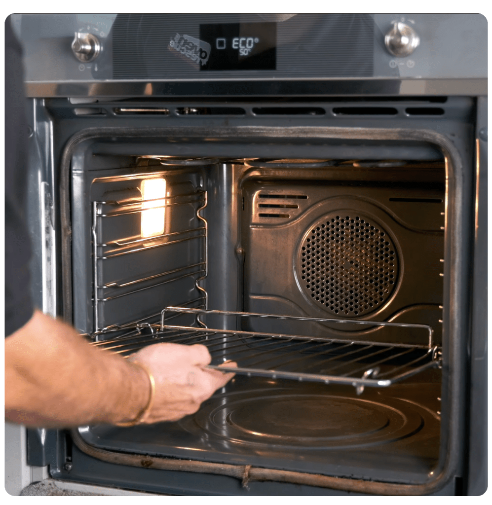 A person adjusts an oven rack inside an illuminated oven. The digital display shows "ECO" at 50 degrees, suggesting energy-efficient use.